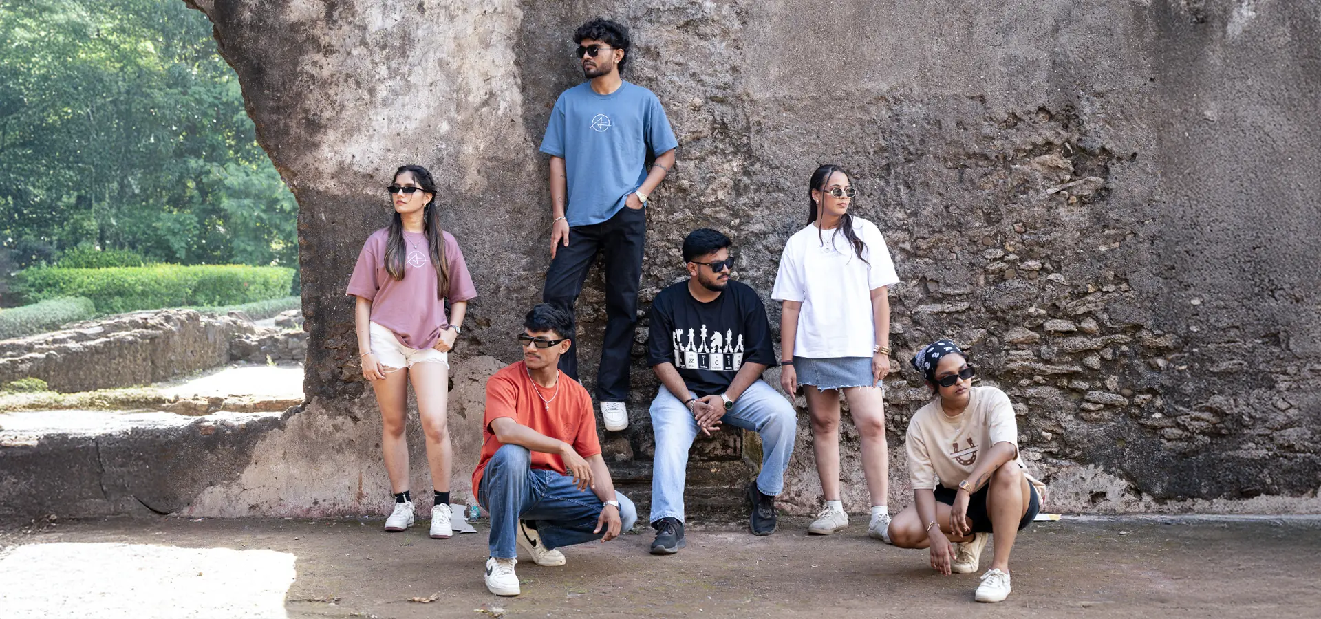 Six models in Fenzzicio tees posing against a weathered stone wall